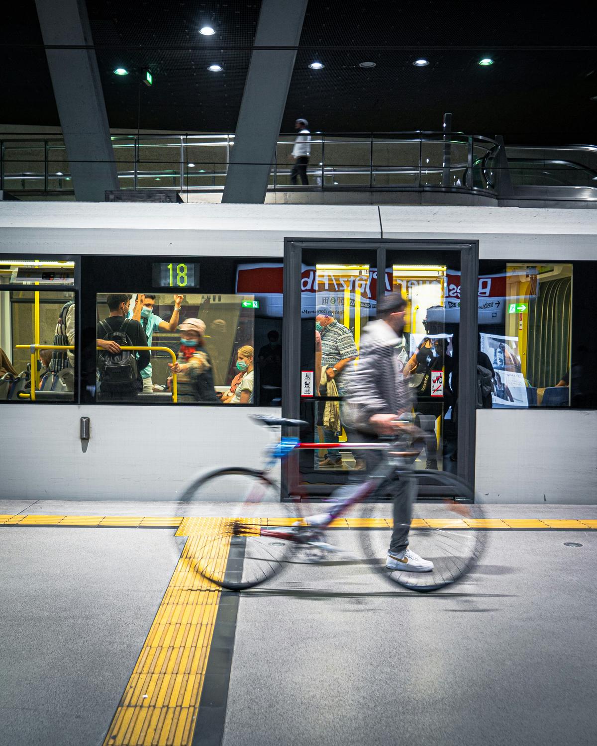 A person riding a bicycle on a dedicated bike lane in a bustling city, with public transportation visible in the background.